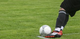 soccer player kicking white gray soccer ball on green grass field