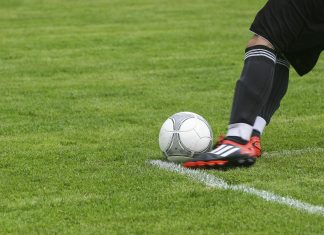 soccer player kicking white gray soccer ball on green grass field