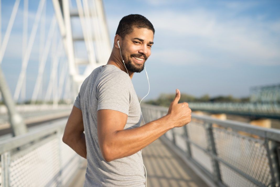 Smiling athlete with earphones holding thumbs up ready for training.
