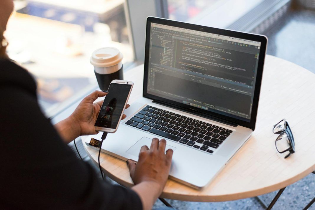 pexels-photo-1181244 person holding smartphone while using laptop