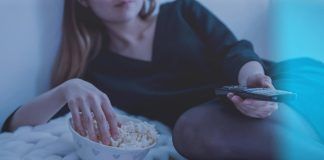 woman in white bed holding remote control while eating popcorn