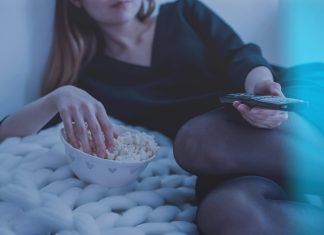 Bagaimana Teknologi Membentuk Hiburan Dalam Talian di Malaysia woman in white bed holding remote control while eating popcorn