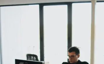 man in black shirt sits behind desk with computers